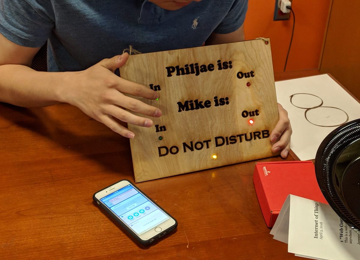 person holding wood sign with lights that show when students are in or out of dorm room