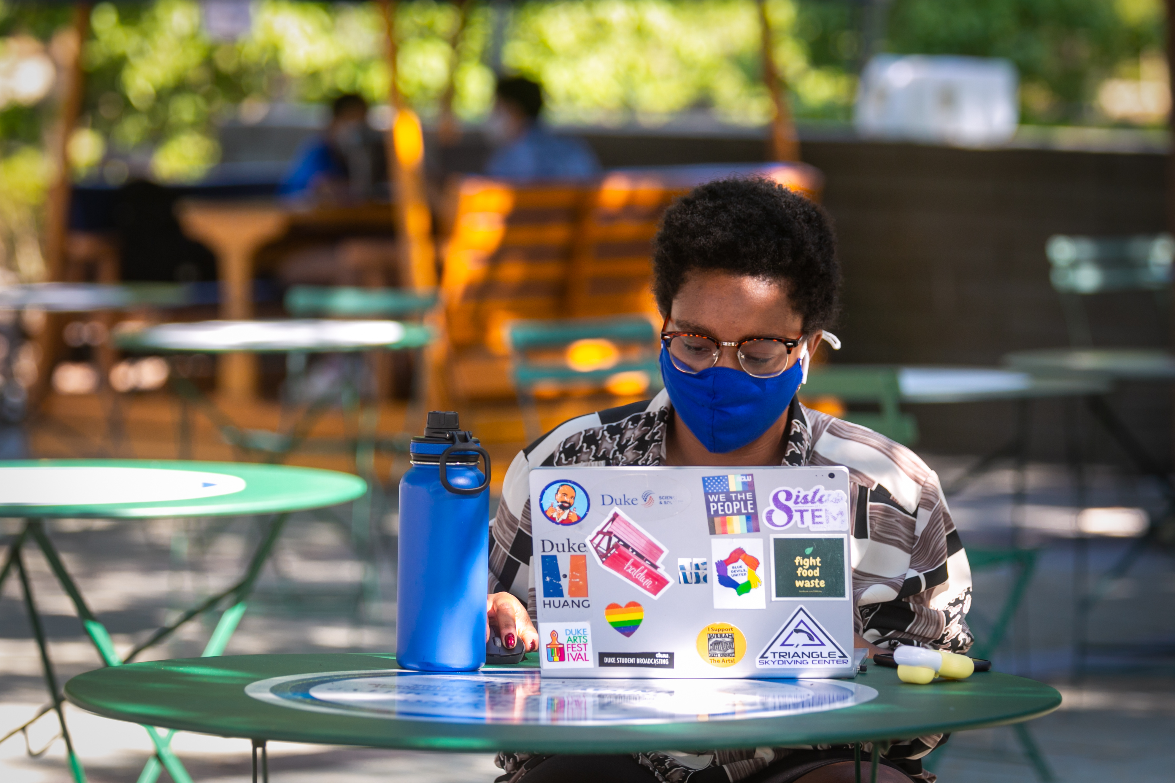 A student works on a computer outside wearing a mask.