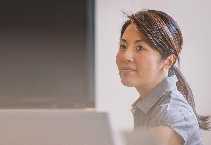 instructor smiling at desk near screen at front of the class