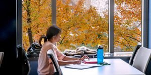 Girl studying by window with fall foliage.