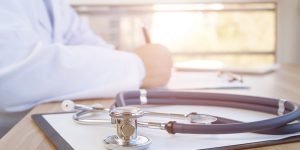 Close-up of stethoscope and folder on background of doctor at desk