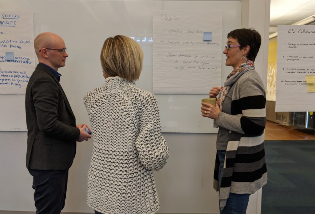 3 faculty discussing course next to large poster