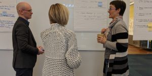 3 faculty discussing course next to large poster