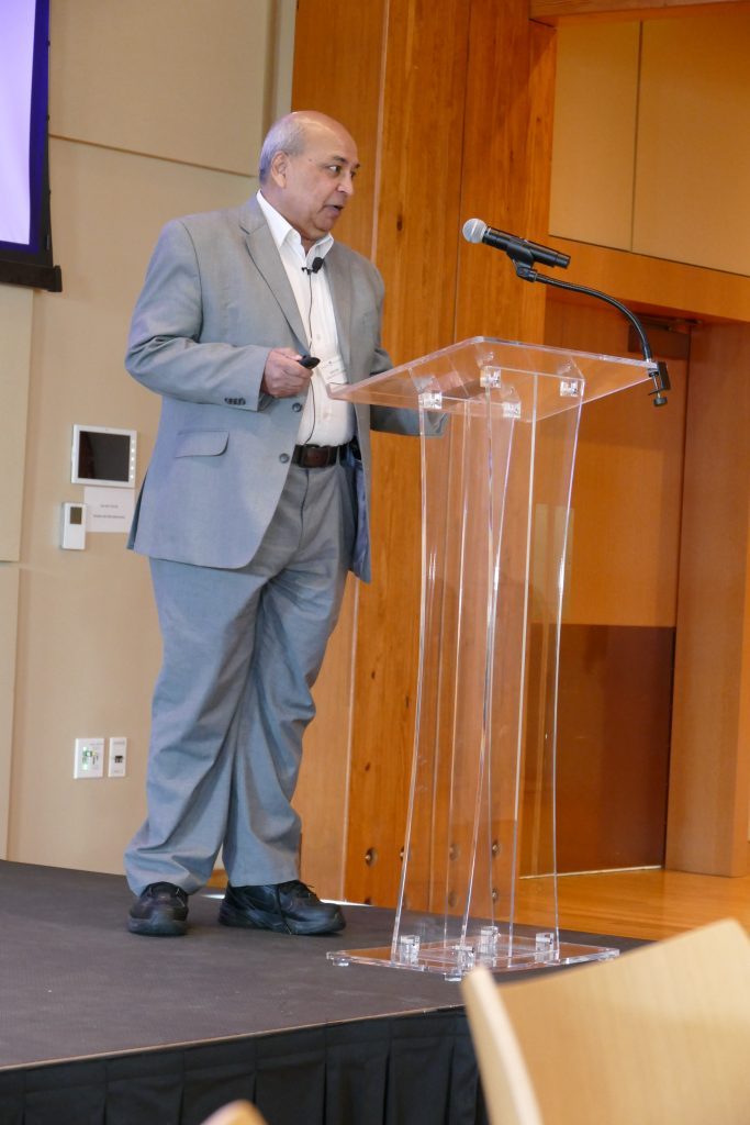 Dr. Goel stands at a clear podium as he delivers his keynote speech.