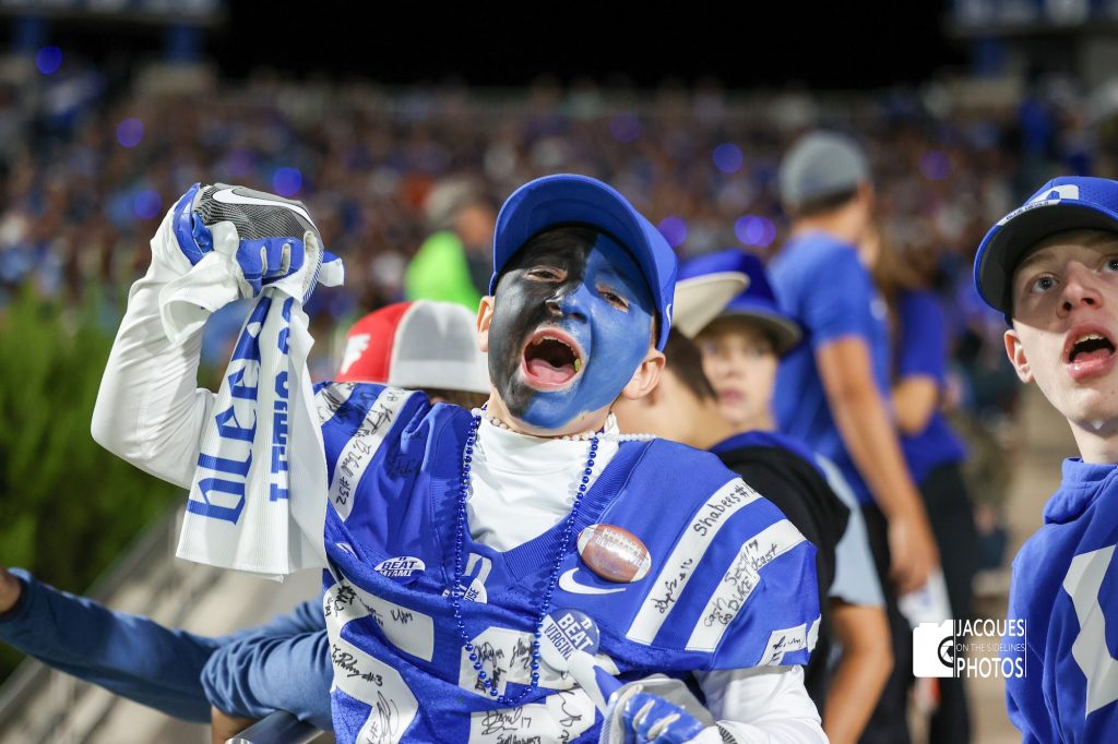 A football player with his face painted in his team's colors shouts in victory.